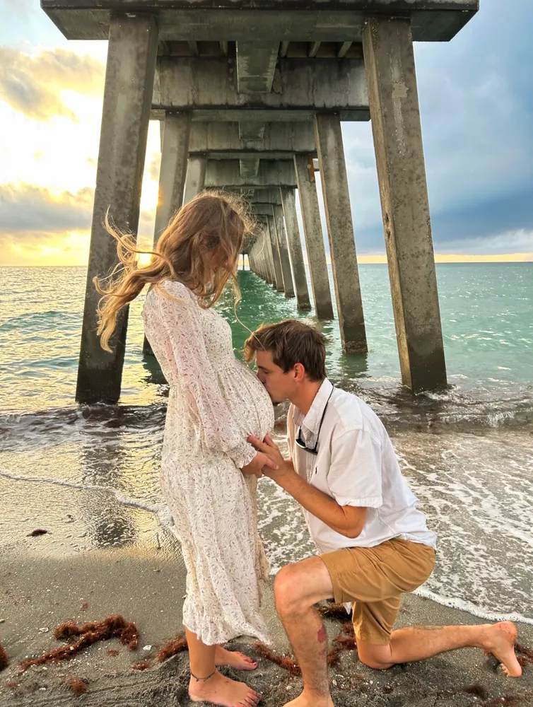 Partner kissing an expecting mother's belly under the pier